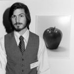 Black and white photograph of a young bearded man seated beside an apple