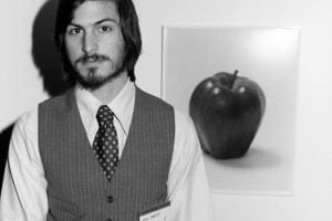 Black and white photograph of a young bearded man seated beside an apple