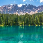 A still turquoise alpine lake below forested mountains