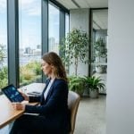 Professional reviewing environmental data on a tablet by large windows with native greenery and rooftop solar panels