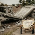 Tilt-shift miniature of a collapsed bridge with engineers at a drawing board tracing the failure back to the design