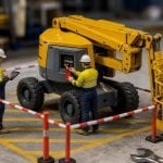 Miniature construction worksite with a boom lift tagged out of service while technicians document a safety defect
