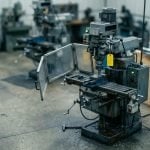Tilt-shift view of a workshop milling machine with its interlock guard swung fully open and the machine still powered up, green run light lit