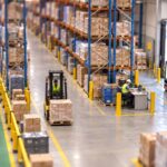 Tilt-shift miniature of an Australian warehouse showing a forklift aisle separated from a marked pedestrian walkway by bollards and guard rail
